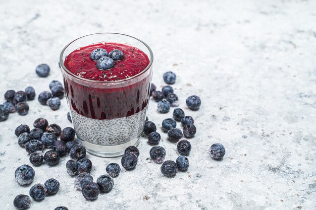 Foto prima colazione o spuntino sana di mattina con i semi ed i mirtilli di chia su fondo di pietra bianco