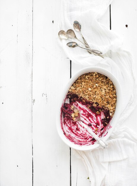 Healthy breakfast Oat granola berry crumble with in ceramic baking dish over white rustic backdrop half eaten