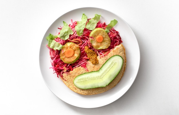 Healthy breakfast. Oatmeal pancake, vegetable salad in the form of a cheerful smiley on a white plate. Top view.