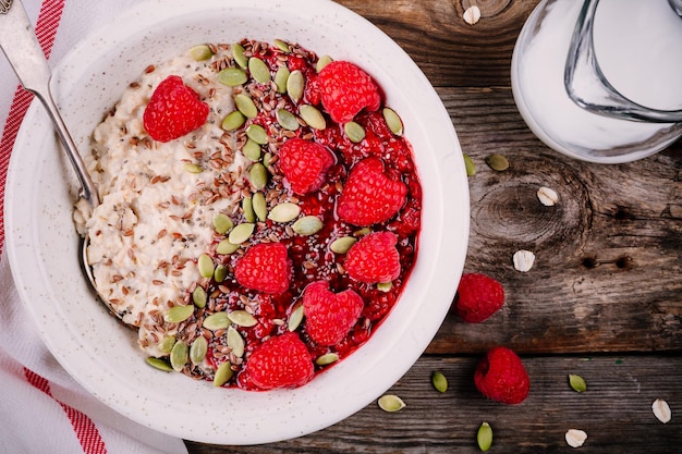 Healthy breakfast oatmeal with fresh raspberries flax seeds and pumpkin seeds on wooden background