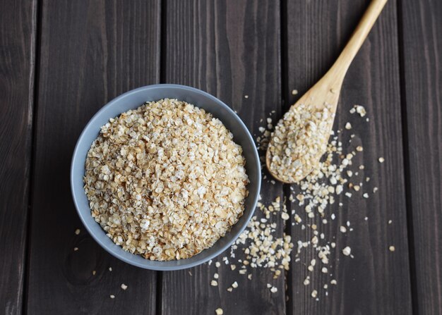 Healthy breakfast rolled oats flakes in ceramic bowl and wooden spoon on dark wooden table, top view