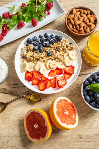 요구르트 muesli 블루베리 딸기와 바나나 접시와 함께 제공되는 건강한 아침 식사. 모닝 테이블 그라놀라 아몬드 열매 감귤 주스와 녹색 허브.