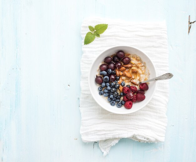 Healthy breakfast set. Bowl of oat porridge with fresh berries, almond and honey over white napkin.