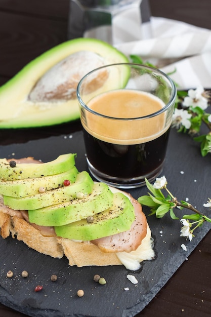 Foto colazione salutare. pane di grano tostato con avocado fresco affettato, prosciutto, formaggio e tazza di caffè