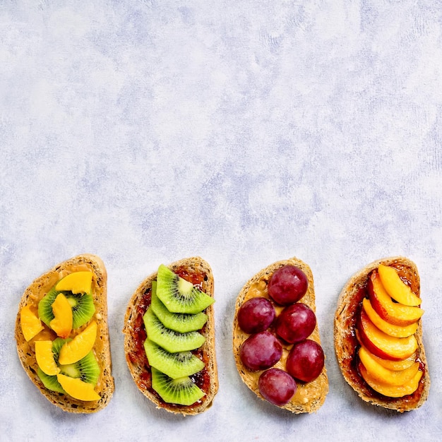 Healthy breakfast toasts with peanut butter strawberry jam banana grapes peach kiwi pineapple nuts Copy space