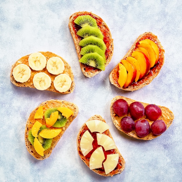 Healthy breakfast toasts with peanut butter, strawberry jam, banana, grapes, peach, kiwi, pineapple, nuts. Copy space