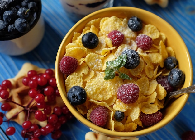 Healthy breakfast with corn flakes berries waffle and milk on blue background