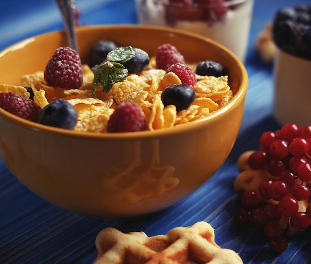 Healthy breakfast with corn flakes berries waffle and milk on blue background