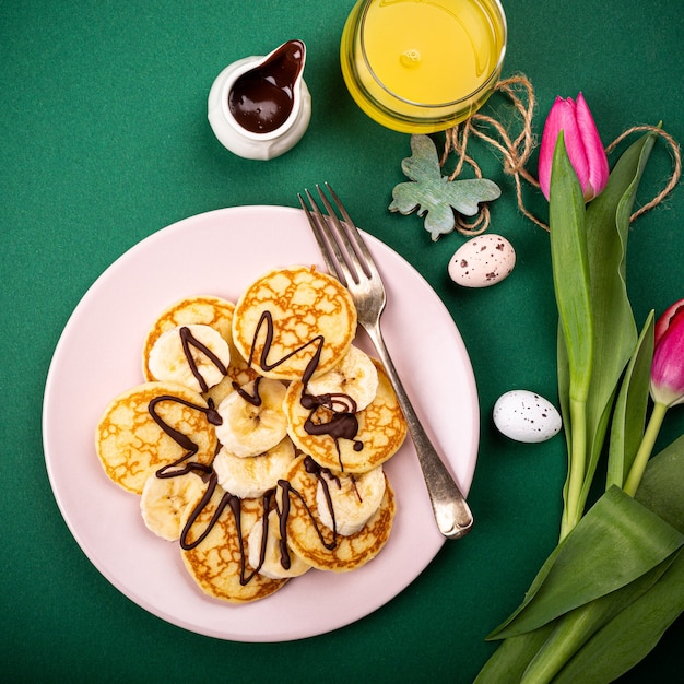 緑の表面にバナナとチョコレートと新鮮なホットパンケーキ、上面図で健康的な朝食