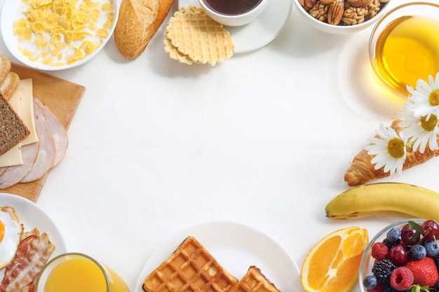 Healthy breakfast with muesli, fruits, berries, nuts, coffee, eggs, honey, oat grains and other on white background. Flat lay, top view, copy space for text, frame