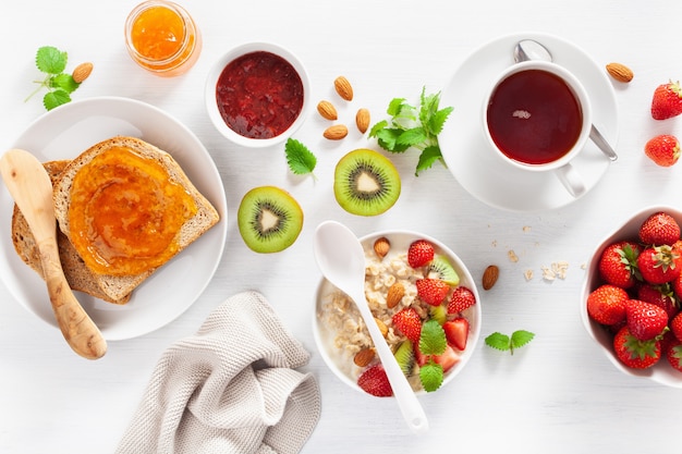 Healthy breakfast with oatmeal porridge, strawberry, nuts, toast, jam and tea. Top view