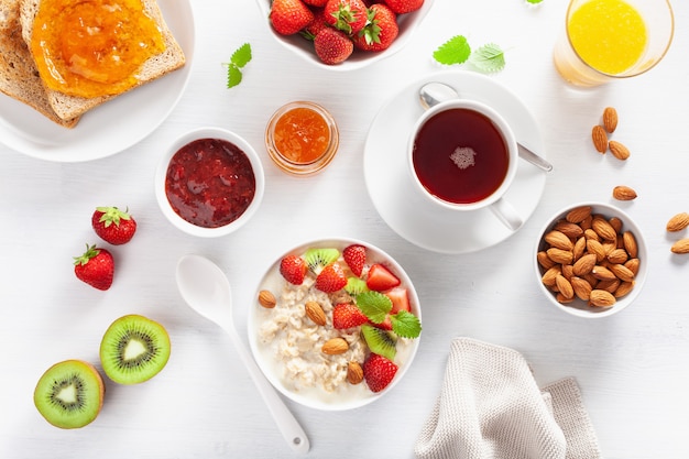 Healthy breakfast with oatmeal porridge, strawberry, nuts, toast, jam and tea. Top view