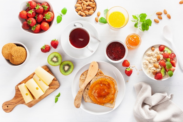 Healthy breakfast with oatmeal porridge, strawberry, nuts, toast, jam and tea. Top view