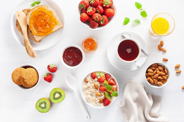 Healthy breakfast with oatmeal porridge, strawberry, nuts, toast, jam and tea. Top view