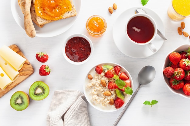 Healthy breakfast with oatmeal porridge, strawberry, nuts, toast, jam and tea. Top view