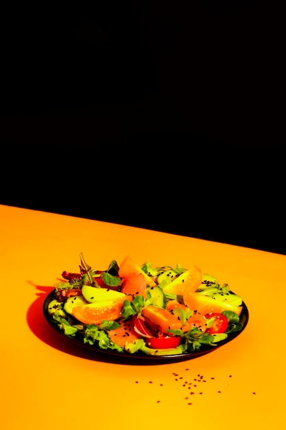 Healthy breakfast with salmon salad with avocado sesame seeds tomatoes mixed herbs and orange juice Contemporary still life orange black background hard light and harsh shadows