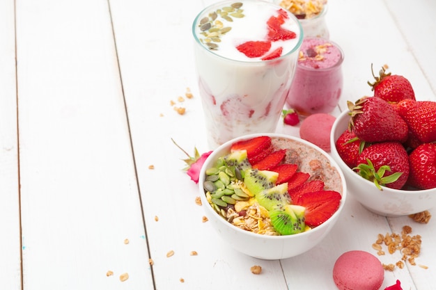 Healthy breakfast with yoghurt, granola and strawberries on white wooden background top view