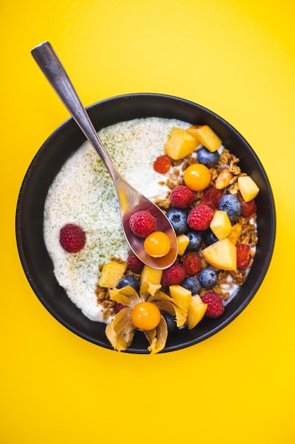 Здоровый завтрак с йогуртом и свежими фруктами и малиной, черникой на желтом фоне