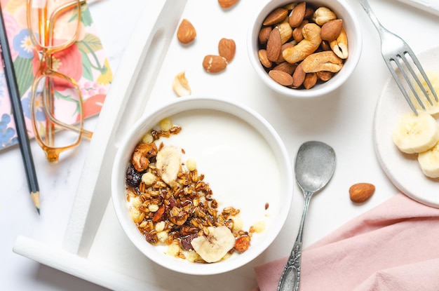 Healthy breakfast with yogurt granola nuts and banana on white table