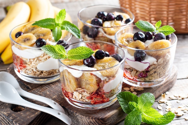 Colazione sana: parfait allo yogurt con muesli, banana e mirtillo su fondo di legno wooden