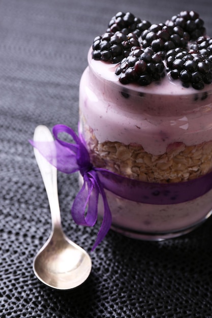 Healthy breakfast yogurt with blackberries and muesli served in glass jar on dark wooden background