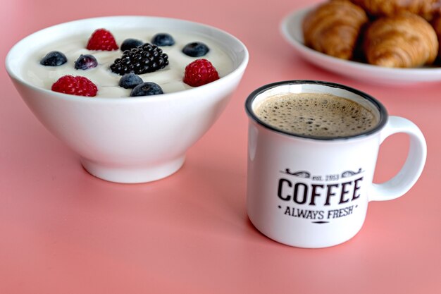 Концепция здорового завтрака с кофейным йогуртом, красными фруктами и круассаном на розовом столе