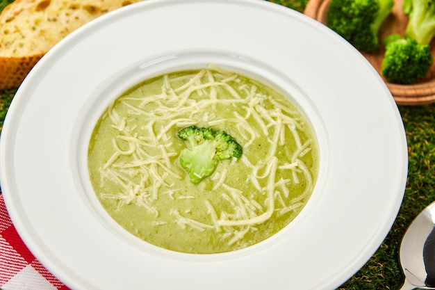 Healthy broccoli cream soup in bowl on green grass