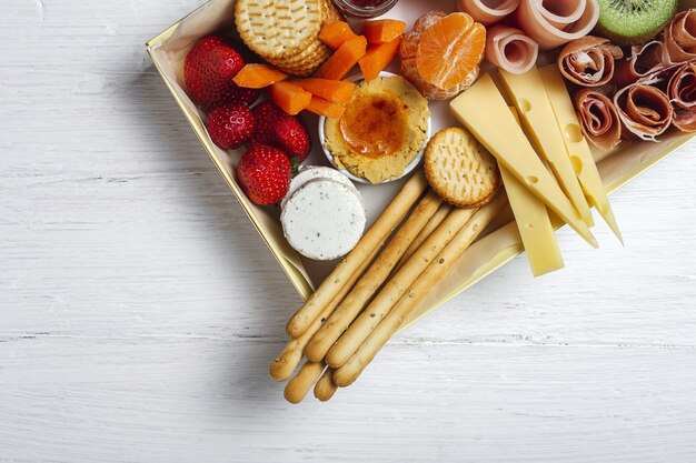 Scatola per brunch sano da asporto con prosciutto, fragole; kiwi; pane; biscotti; formaggio, carote, mandarini, hummus.