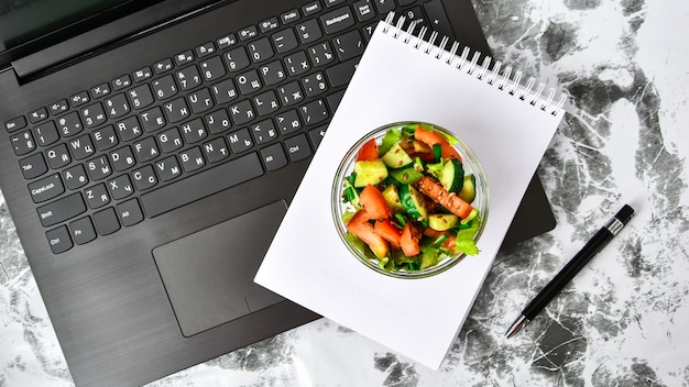 Здоровая закуска бизнес-ланча в офисе, овощной салат, пустой блокнот с ручкой