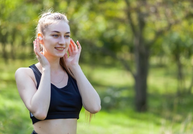 Healthy cheerful fit woman listening to music in headphones in the park