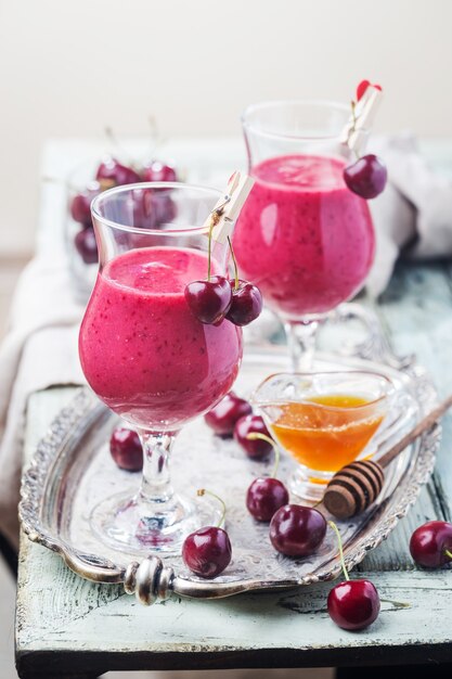 Frullato di ciliegia sano con fragole congelate, acqua di cocco e miele in vetro sulla tavola di legno bianca.