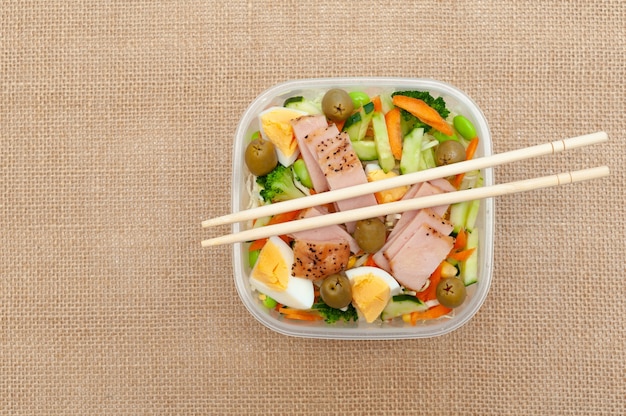 Healthy chicken salad with vegetables in plastic container with chopstick