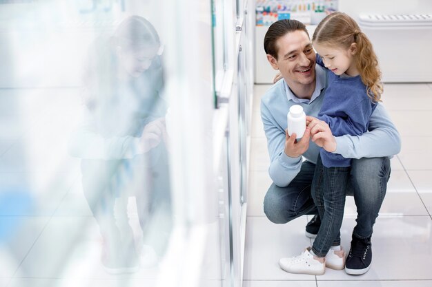 Healthy child. Nice beautiful girl staying while man elevating bottle with medication