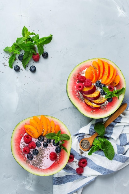 Healthy clean eating dieting and nutrition seasonal summer breakfast concept Fruit salad with yogurt in carved watermelon bowl on a kitchen table Top view flat lay background