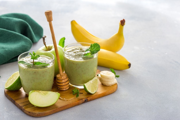 Cibo pulito sano, tazza di vetro con frullato di salute verde di mela spinaci lime e miele su un tavolo