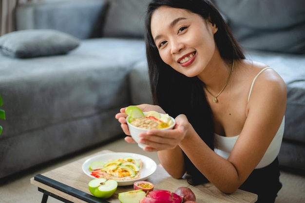 健康的なきれいな食品のコンセプト、ダイエットライフスタイルのための新鮮な野菜を持つアジアの女性、家で有機的な食事を食べる幸せな菜食主義の女性の女の子