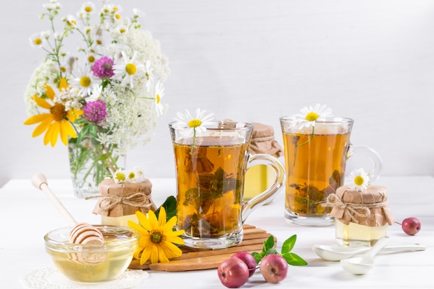 A healthy Cup of  herbal tea, a jar of honey and wild flowers. on white surface