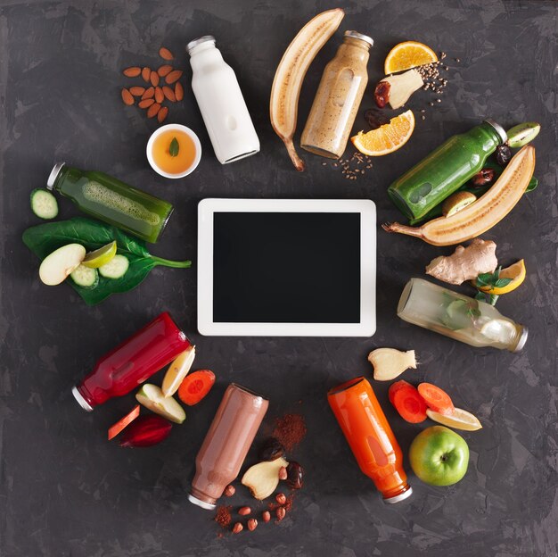 Foto bevande disintossicanti sane con ingredienti di frutta e verdura e tablet. bottiglie di vetro con frullato, vista dall'alto, piatto. concetto online di ordine internet