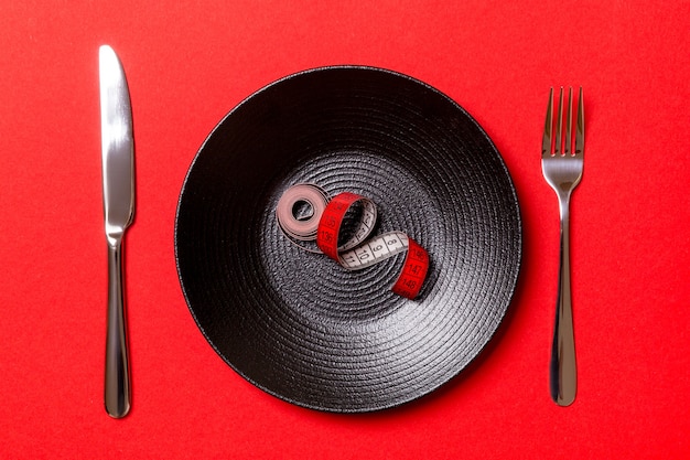 Healthy diet concept of plate with measuring tape, fork and knife on red background. Top view.