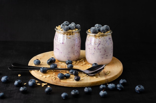 Healthy diet eating. Jars of homemade yogurt with blueberries and oats on wooden board and black . Front view,copyspace