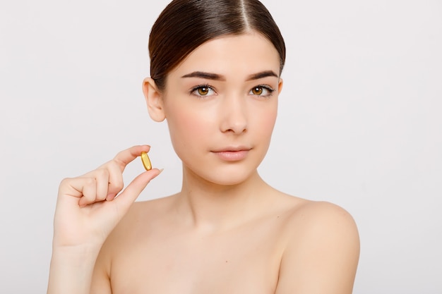 Healthy diet food. Beautiful smiling young woman holding a fish oil pill in her hand. Closeup. taking capsule. Vitamin and dietary supplements