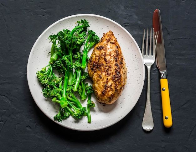 건강한 다이어트 점심 구운 닭 가슴살과 삶은 브로콜리 양배추를 어두운 배경에서 볼 수 있습니다.
