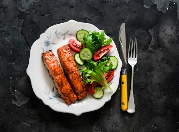 Healthy diet lunch teriyaki sauce baked salmon and fresh vegetable salad on a dark background top view