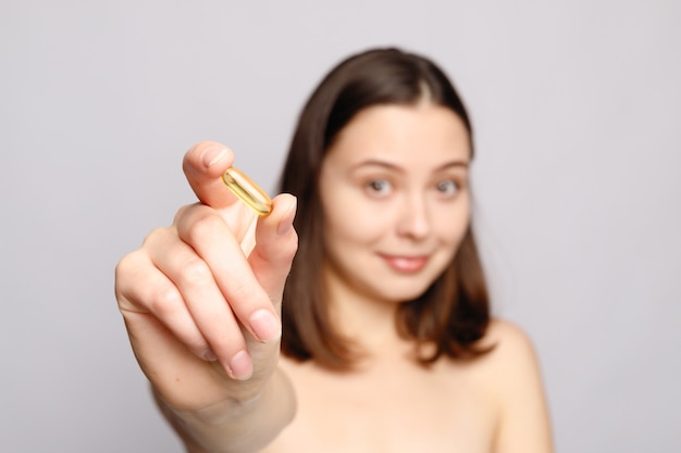 健康的な食事の栄養。魚の油の丸薬を手に持って美しい笑顔の若い女性