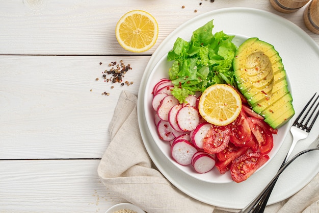 Healthy diet salad with avocado, radish and tomatoes on a white wooden table.