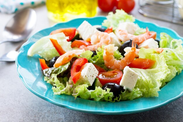 healthy and dietary food greek salad with shrimps and vegetables on a light stone or slate table