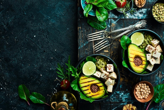 Healthy dinner or lunch Vegetarian food in a bowl avocado tofu cheese flax pumpkin seeds and spinach The concept of healthy eating On a black stone background Top view