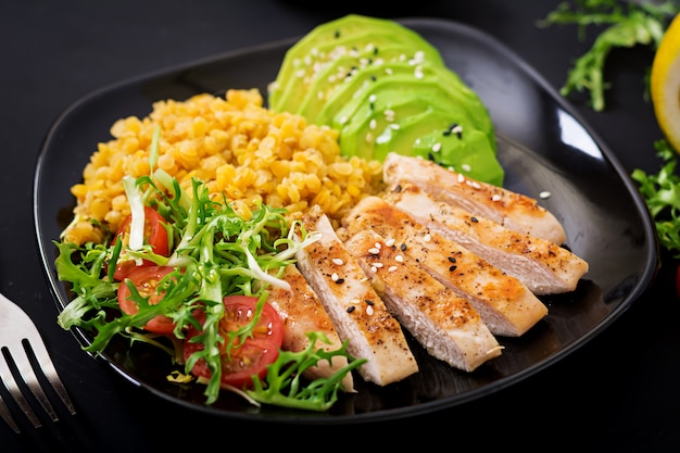 Healthy dish with chicken, tomatoes, avocado, lettuce and lentil on dark  table.