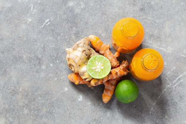 Healthy drink from turmeric and ginger roots and lime in small bottles on grey concrete wall with copyspace.