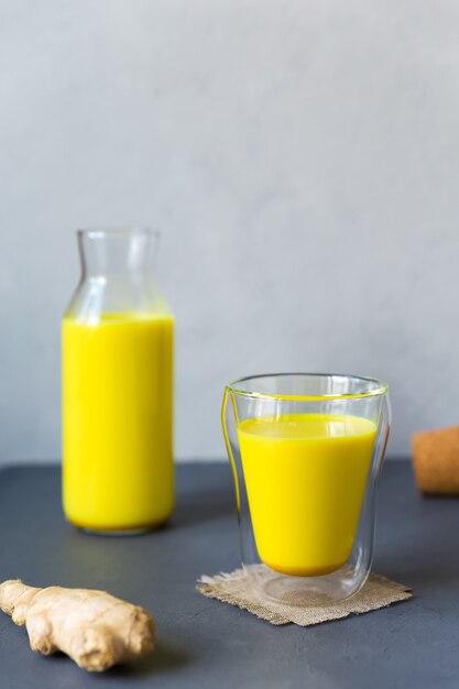 Healthy drink from turmeric powder golden milk in glass and bottle on gray background with copy space